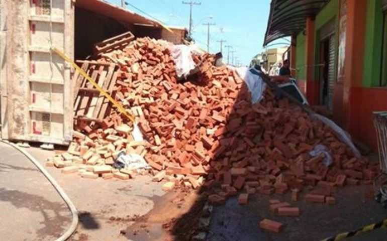 Caminhão carregado com tijolos tomba sobre carro que 'desaparece'